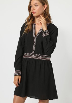 Vestido negro con mangas largas, escote en V y intrincados patrones bordados en rosa y blanco en el cuello y los puños.