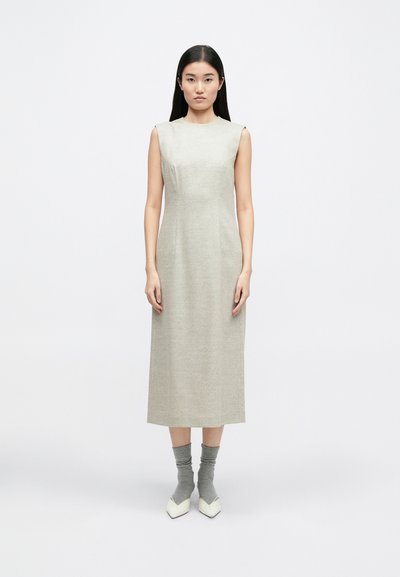 Αμάνικο ανοιχτό γκρι φόρεμα με ευθεία σιλουέτα, σχεδίαση μέχρι το γόνατο, φτιαγμένο από υφαντό ύφασμα. Συνδυάζεται με γκρι κάλτσες και λευκά γοβάκια.
