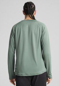 Hosszú ujjú sportpóló tompa zöld színben, texturált anyaggal, kerek nyakkal és ergonomikus varrásokkal a fokozott mozgás érdekében.