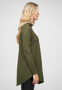 Haut à manches longues vert olive avec un col montant et un ourlet asymétrique. Texture douce, manches ajustées et silhouette décontractée.