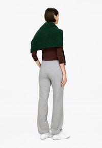 Green knitted wrap draped over a brown long-sleeve top, paired with gray sweatpants and white sneakers. Model is viewed from behind.