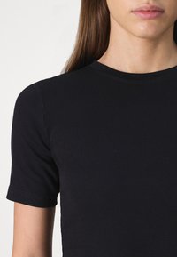 Svart ribbet t-skjorte med kort arm og rund hals. Stoffet ser glatt og tettsittende ut, med subtile sømdetaljer i kantene.
