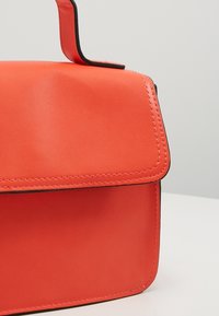 Sac à main en cuir rouge au design structuré, avec une fermeture à rabat et des coutures noires contrastantes. Surface lisse avec une forme arrondie.