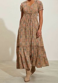 Maxi šaty v hnědých tónech s paisley vzorem, krátkými nabíranými rukávy a zvýrazněným pasem. V kombinaci s béžovými kotníkovými botami.