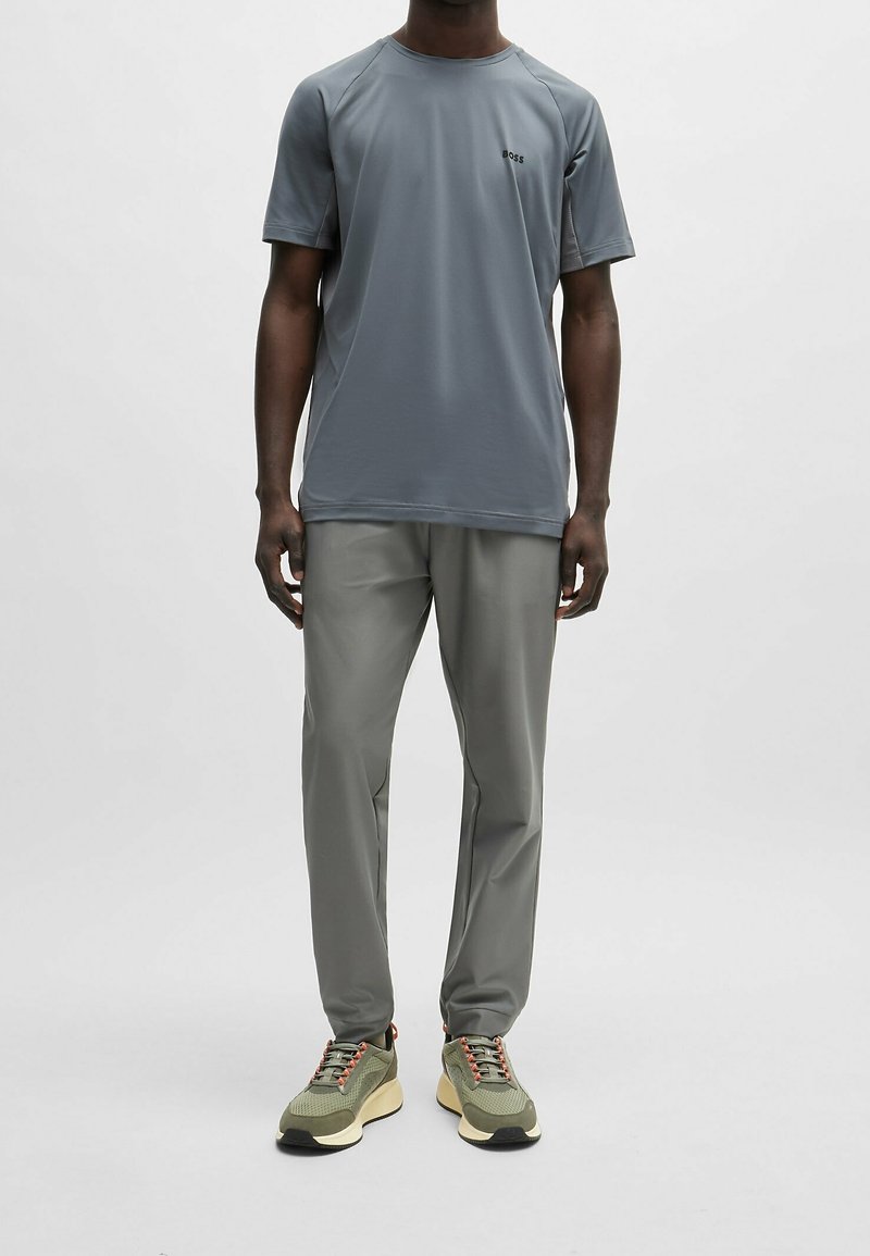 Grijze sportieve t-shirt met korte mouwen en een subtiel logo, gecombineerd met grijze broek en groene sneakers met een textuurdesign.