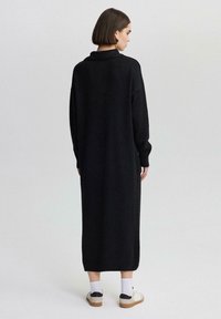 Abito nero in maglia con colletto alto, maniche lunghe e vestibilità ampia, che arriva fino alle caviglie. Le finiture a costine ai polsini e all'orlo aggiungono texture.