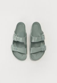 Sandales en plastique vert avec deux boucles réglables, une semelle ergonomique et une finition lisse et mate. Conçues pour le confort et la facilité d'utilisation.