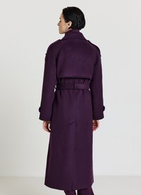 Lungo cappotto di lana viola con vita cintata, spalle con epaulette e spacco sul retro. Tessuto liscio e design su misura.