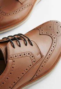 Chaussures en cuir marron avec des perforations, au design brogue, lacets standard et semelle légère contrastante.