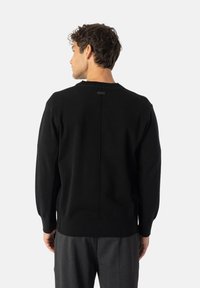 Fekete pulóver texturált kötött anyagból, kerek nyakkivágással, bordás mandzsettákkal és egy kis címkével a hátsó középen.