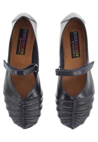 Scarpe in pelle nera con design plissettato, punta arrotondata e cinturino regolabile. L'interno presenta un'etichetta di marca colorata.