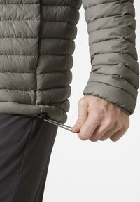 Puffjacke in gedämpftem Grau mit gestepptem Design. Eine Hand zieht am Kordelzug am Saum zur Anpassung der Passform.