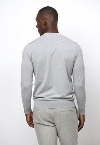 Maglione grigio in cotone a collo rotondo con polsini e orlo a costine. Presenta una texture liscia e un design aderente, indossato con pantaloni su misura grigi chiari.