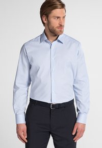 Camicia a righe blu chiaro con maniche lunghe, colletto a punta, chiusura con bottoni e tessuto liscio, indossata con pantaloni scuri e cintura.