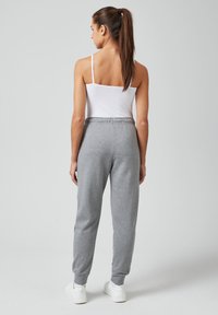 Hellgraue Sweatpants aus weichem Material, mit einer lockeren Passform, einem elastischen Bund und gerippten Bündchen. Kombiniert mit einem weißen Tank-Top.