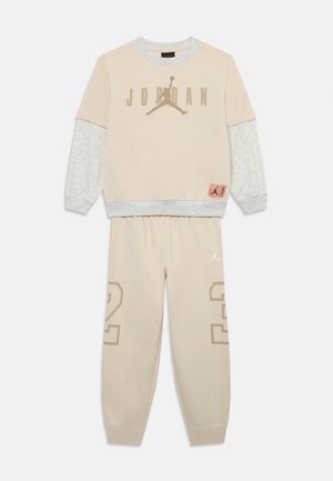 Sweatshirt beige avec des manches grises, arborant le logo "JORDAN" et l'emblème Jumpman. Pantalons de jogging beige coordonnés avec "23" imprimé sur la jambe.