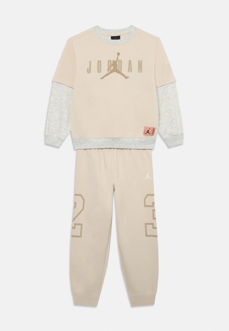 Sudadera beige con mangas grises, que presenta el logo "JORDAN" y el emblema de Jumpman. Pantalones de chándal beige a juego con el "23" impreso en la pierna.
