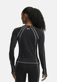 Zwart sporttop met lange mouwen, voorzien van meshpanelen, witte stiksels en een aansluitend ontwerp, geschikt voor sport of workouts.