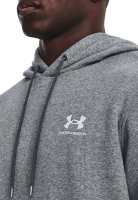 Grå hoodie med tekstureret stof, der har en frontlomme og justerbar snor i hætten. Broderet Under Armour-logo på brystet.