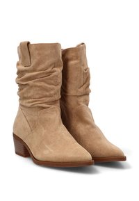 Par de botas de ante color beige hasta el medio de la pantorrilla, con cañas caídas, punteras afiladas, tacones bajos y apilados, y tiradores laterales.