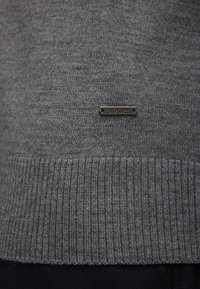Gray sweater with a smooth knit texture and ribbed hem, featuring a small, silver "JOOP!" logo tag near the bottom.