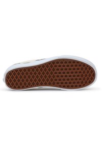 Suela de zapatilla blanca con una textura de goma marrón, que presenta un dibujo en forma de diamante para un mejor agarre, bordeada por un suave borde blanco.