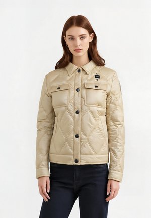 Veste matelassée beige avec un devant à boutons, deux poches poitrine et une coupe légèrement ajustée. Présente des boutons noirs et un écusson sur la manche.