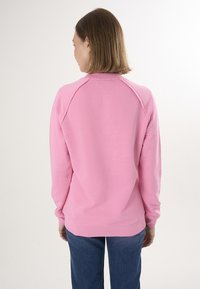 Felpa rosa chiaro con scollatura rotonda, maniche raglan e polsini a coste. Abbinata a jeans in denim blu a gamba larga.