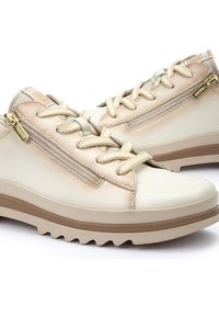 Baskets en cuir beige avec des accents texturés, un design à lacets, une fermeture éclair sur le côté et une semelle en caoutchouc avec un motif cranté.