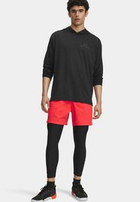 Zwarte hoodie met lange mouwen, neonroze shorts, zwarte leggings en zwarte sport schoenen met oranje accenten. Minimalistische branding op de top.