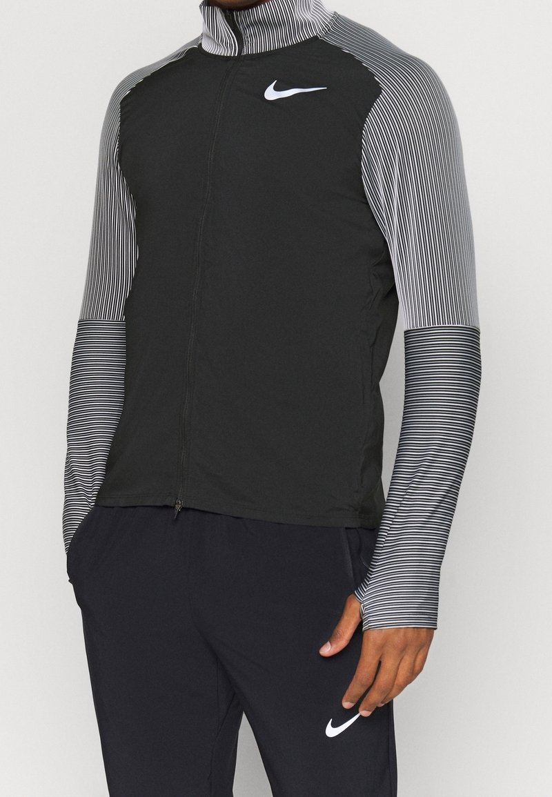 Nike zip-up jacket met een zwarte body en gestreepte grijze mouwen. Gemaakt van lichtgewicht materiaal met een hoge kraag en logo-details.