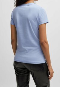 Ljusblå bomulls-t-shirt med korta ärmar, rund halsringning, slät textur och figursydd passform. Bärs med glänsande svarta läderbyxor.