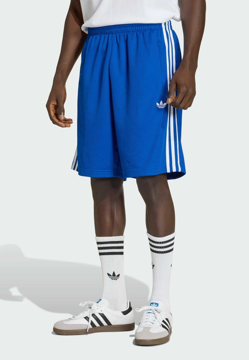 Shorts de sport bleus avec des rayures blanches, en tissu mesh, associés à des chaussettes blanches à rayures noires et des baskets blanches avec des accents noirs.