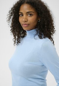 Pull bleu clair à col roulé en matière douce, avec une coupe ajustée et des accents côtelés au col et aux poignets.