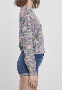 Maglione lavorato a maglia multicolore con maniche lunghe e un design cropped, caratterizzato da un motivo texture in tonalità pastello, abbinato a pantaloni shorts in denim blu.