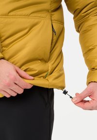 Una giacca isolante giallo senape presenta una cerniera e un cordoncino regolabile, con una texture liscia e un design leggermente imbottito.