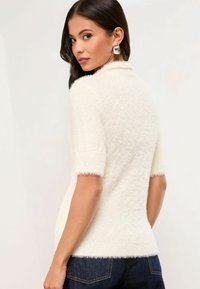 Top blanco de manga corta hecho de tela suave, con un diseño ajustado y una textura suave. Con cuello y bordes acabados.