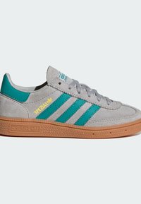 Grijze suede sneaker met teal strepen en gele logo. Voorzien van een gestructureerde gumrubberen zool en grijze veters. Klassiek low-top ontwerp.