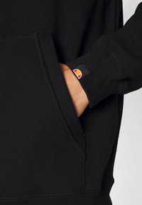 Zwarte sweatshirt met een kangoeroezak, geribde manchetten en een klein multicultureel logo label op de mouw. Zachte stoftextuur.