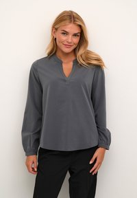 Šedá blůza s dlouhými rukávy a výstřihem do V, s nařasenými manžetami a volným střihem. Hladká textura, minimalistický design a bez viditelných vzorů.