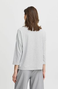 Grijze, losvallende langemouwen shirt met een zachte textuur, brede halslijn en afhangende schouders, gecombineerd met lichtgrijze op maat gemaakte broek.