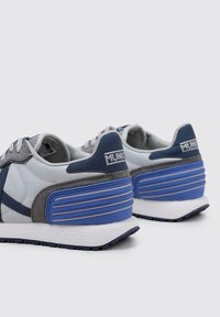 Zapatillas deportivas en gris y azul con un upper texturizado, paneles en contraste y un diseño de tacón acanalado prominente. Presentan cordones y acentos de logo.
