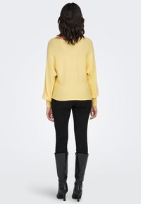 Gele gebreide trui met een losse pasvorm en ribbelige textuur, gecombineerd met zwarte skinny jeans en zwarte laarzen tot aan de knie.