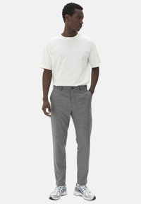 Pantalons grisés à motifs avec une coupe ajustée, associés à un t-shirt blanc uni et des chaussures de sport grises avec des accents bleus.