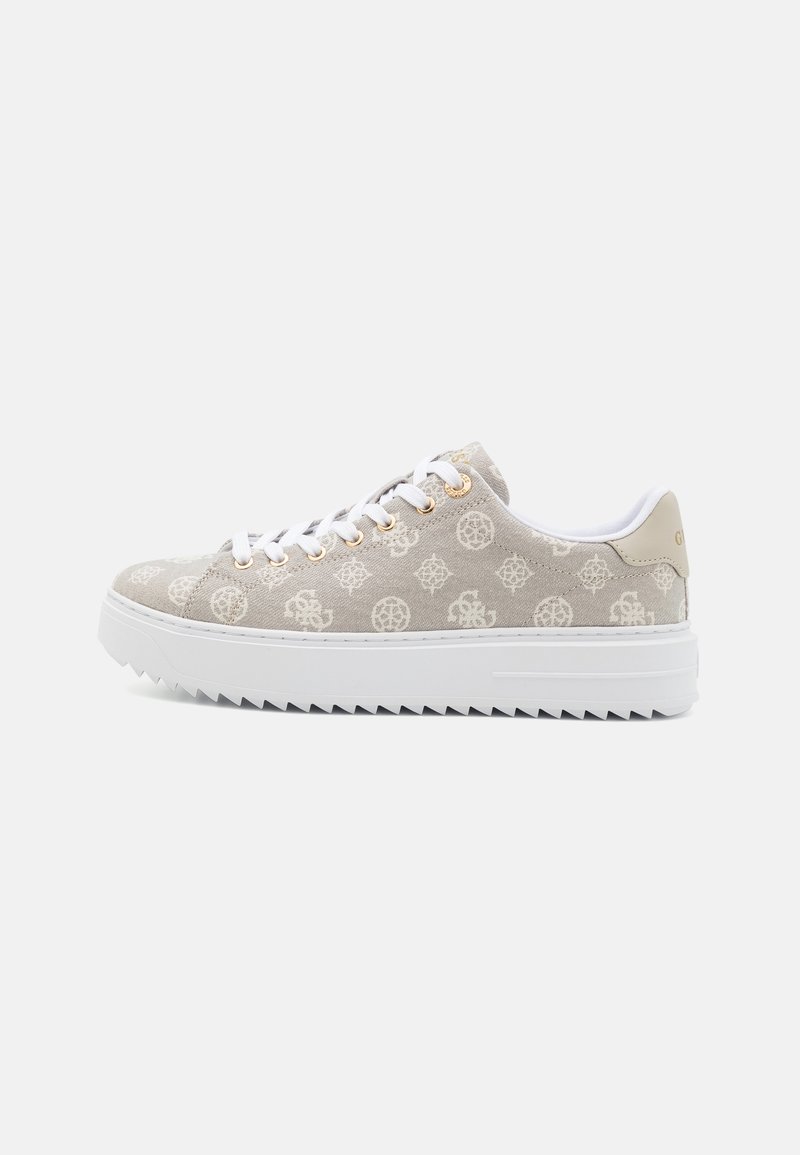 Basket basse beige avec lacets blancs, œillets dorés, tissu à motifs, semelle blanche épaisse striée et languette beige au talon sur fond uni.