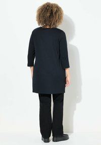 Mustat tunikatopit, joissa on kolme neljästä hihoista, sileä rakenne ja pyöreä helma, yhdistettynä mustiin suoriin housuihin ja paksupohjaisiin kenkiin.