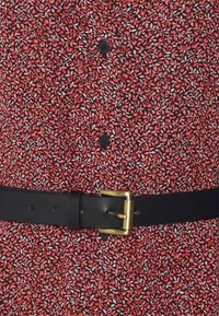 Röd och svart blommönstrad skjorta med svarta knappar, tillsammans med ett svart läderbälte med en guldtonad spänne.
