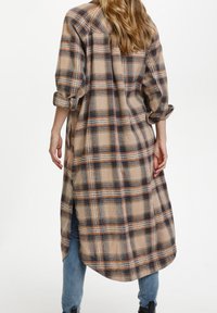 Lång rutig skjorta i beige, marinblått och orange med uppvikta ärmar, sidospjäll och avslappnad passform, tillverkad av mjukt bomullstyg.