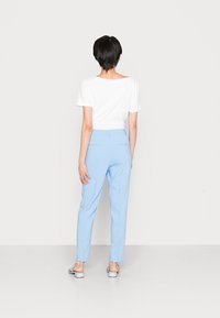 Pantaloni azzurri chiari con una vestibilità affusolata e due tasche posteriori, abbinati a una maglietta bianca semplice, visti da dietro.