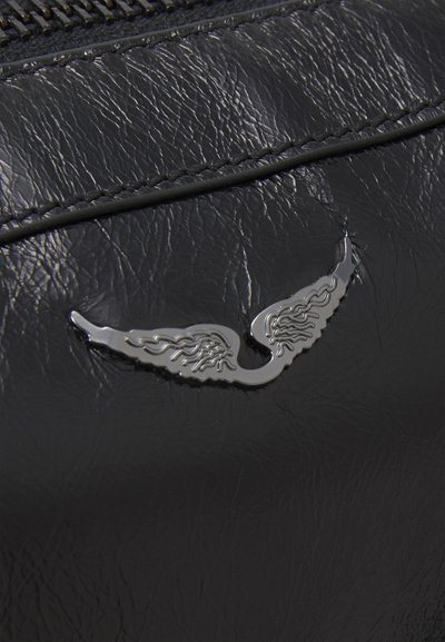 Matériau en cuir noir avec une texture visible, mettant en avant un emblème argenté en forme d'aile. Des coutures détaillées longent les bords.